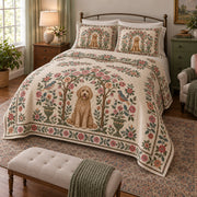 A curly goldendoodle sits inside an airy rose bower with small pink blossoms, green leaves and a decorative folk border on a quilt set with two matching shams, angled view.