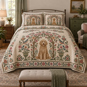 A curly goldendoodle sits inside an airy rose bower with small pink blossoms, green leaves and a decorative folk border on a quilt set with two matching shams, front view.