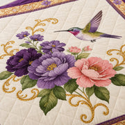 Close-up of hummingbird, purple and pink flowers, green leaves and gold scrollwork on the quilt