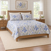Periwinkle iris quilt set on a long oak bed, left angle view