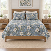 Dusty denim dogwood quilt set on a long oak bed, front hero view