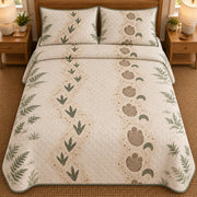 AI mockup, high overhead bedroom view of a dinosaur quilt with two decorative dinosaur footprint trails in sage and tan framed by ferns and two matching printed pillow covers.