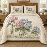 AI mockup, front bedroom view of a hydrangea quilt with hydrangeas arranged in three glass vases and two matching printed pillow covers.