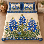 AI mockup, high centered overhead view of bluebonnet flower spikes with green foliage on ivory with a blue floral border, quilt and two matching printed pillowcases in a neutral bedroom.