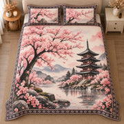 AI mockup, high centered overhead view of pink cherry blossoms framing a lakeside Japanese pagoda and misty mountains, quilt and two matching printed pillowcases in a neutral bedroom.