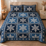 AI mockup, front view of large ivory snowflakes in varied navy and blue patchwork squares, quilt and two matching printed pillowcases in a neutral bedroom.