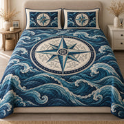AI mockup, front view of a large ivory and teal compass rose amid rolling navy blue ocean waves, quilt and two matching printed pillowcases in a neutral bedroom.